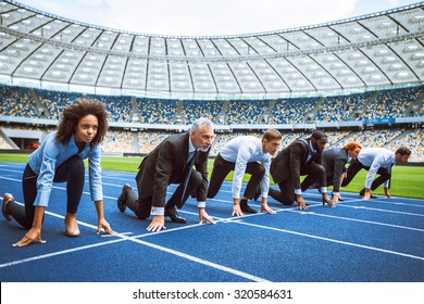 Side View Photo Of Confident Multi Ethnic Business People Lined Up Getting Ready For Race On Modern Sport Track. Stadium As A Background