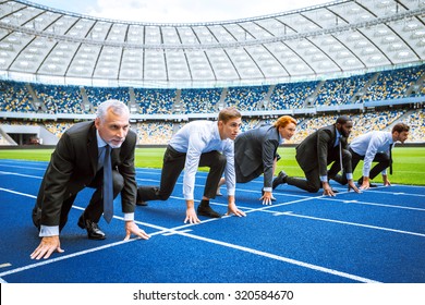 Side View Photo Of Confident Multi Ethnic Business People Lined Up Getting Ready For Race On Modern Sport Track. Stadium As A Background