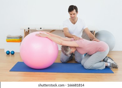 Side view of a physical therapist assisting senior woman with yoga ball in the gym at hospital - Powered by Shutterstock