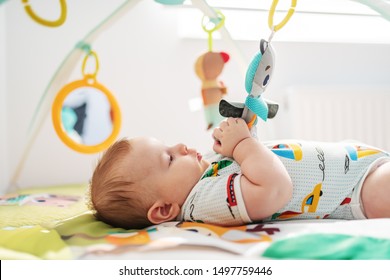 Side view of playful Caucasian chubby six months old baby boy in colorful bodysuit playing with crib toys. - Powered by Shutterstock - Get 15% off with code: PIKWIZARD15