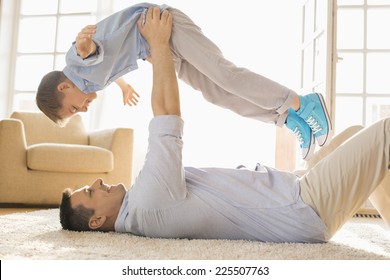 Side View Of Playful Father Lifting Son While Lying On Floor At Home