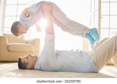 Side View Of Playful Father Lifting Son While Lying On Floor At Home