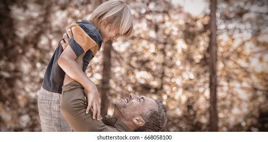 Side View Of Playful Father Lifting Up Son In Forest