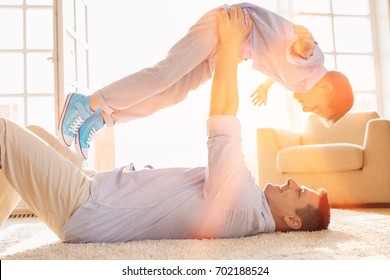 Side View Of Playful Father Lifting Son While Lying On Floor At Home