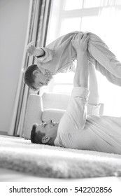 Side View Of Playful Father Picking Up Son While Lying On Floor At Home