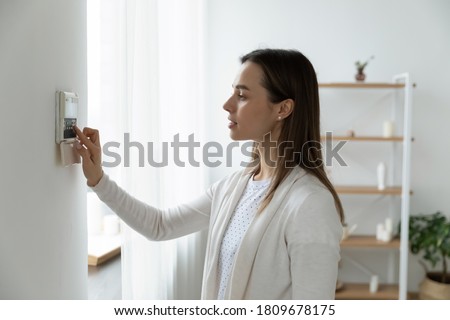 Side view pleasant young woman using smart home system or activating modern alarm system before leaving apartment. Happy lady turning off easy security technology, when returning house or flat.