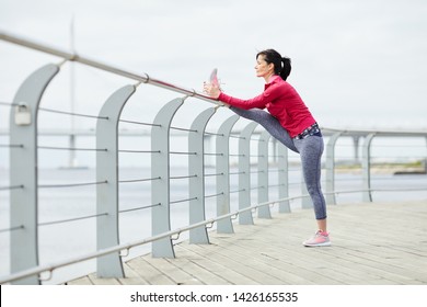 Side view portrait of active mature woman stretching legs outdoors while jogging on pier, copy space - Powered by Shutterstock