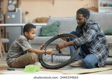 Side view portrait of African American father and son repairing bicycle wheel together sitting on floor at home - Powered by Shutterstock