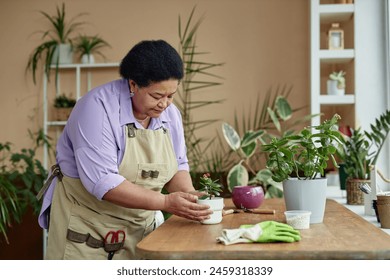 Side view portrait of African American senior woman repotting green plant with care and enjoying gardening at home, copy space - Powered by Shutterstock