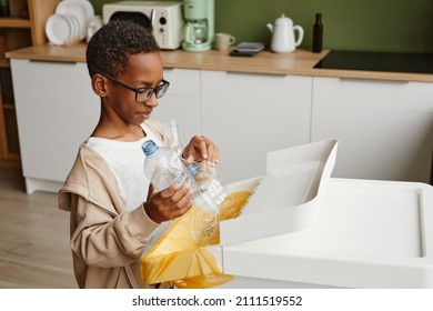 Side view portrait of African-American boy putting plastic bottles in recycling bins while sorting household waste at home, copy space - Powered by Shutterstock