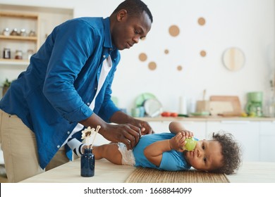 Side View Portrait Of African-American Father Changing Diaper To Cute African-American Toddler Eating Apple, Copy Space