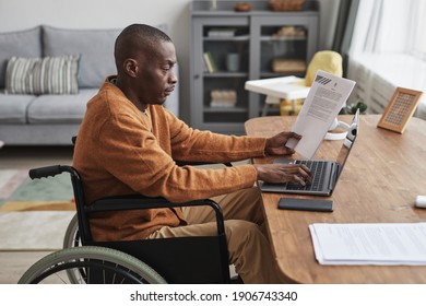 Side view portrait of African-American man using wheelchair working from home in minimal grey interior, copy space - Powered by Shutterstock