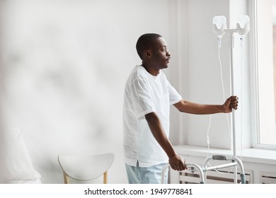 Side view portrait of African-American man in hospital holding onto iv drip stand and looking at window pensively, copy space - Powered by Shutterstock