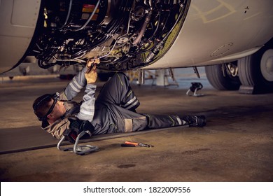 Side View Portrait Of Airplane Maintenance Mechanic Inspecting On Aircraft Engine In Aviation Hangar