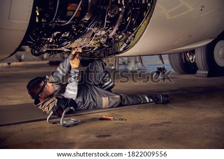 Side view portrait of airplane maintenance mechanic inspecting on aircraft engine in aviation hangar
