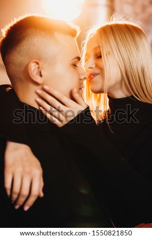 Side view portrait of a attractive young couple smiling before kissing while sitting against a warm light.