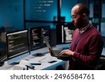 Side view portrait of bearded adult man as computer programmer holding open laptop in IT and cybersecurity office with blue lights copy space