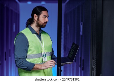 Side view portrait of bearded network technician working with servers in neon light, copy space