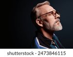 Side view portrait of bearded senior man wearing glasses on dark background, copy space