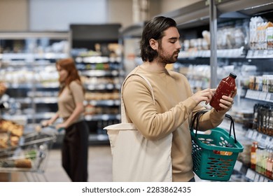 Side view portrait of bearded young man shopping in supermarket and reading ingredients label, copy space - Shutterstock ID 2283862435
