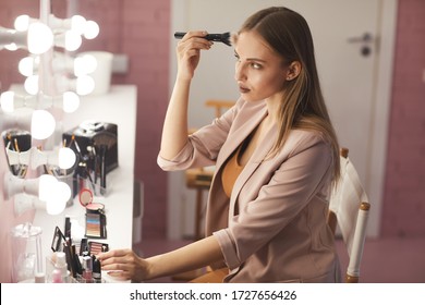 Side View Portrait Of Beautiful Young Woman Putting On Makeup While Looking At Vanity Mirror In Pink Boudoir Interior, Copy Space