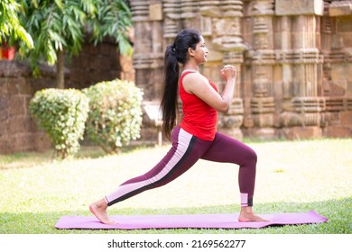 Side view portrait of beautiful young girl wearing red tank top working out at park, doing yoga exercise. Standing in Warrior one pose, Virabhadrasana. Full length - Powered by Shutterstock