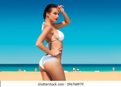 Seitenbild einer schönen jungen Frau in weißem Bikini mit blauem Himmel und Ozean im Hintergrund