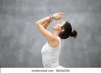 Side view portrait of beautiful young woman wearing sport watch for heart rate and calorie burn control working out against grey wall, doing yoga or pilates exercise. Close up 