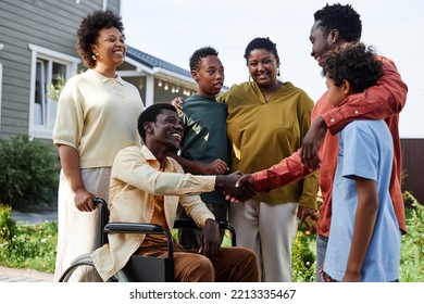 Side view portrait of big African American family with person in wheelchair welcoming guests for Summer party