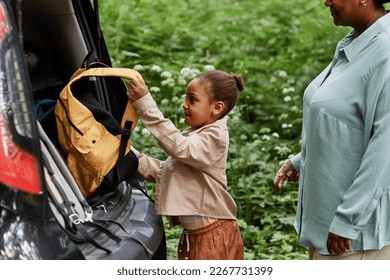 Side view portrait of black little girl putting backpack in car trunk while travelling with mom - Powered by Shutterstock