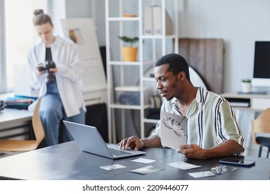 Side View Portrait Of Black Male Photographer Using Laptop For Photo Editing In Minimal Studio Setting, Copy Space