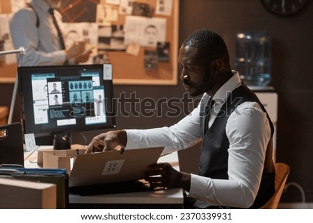 Side view portrait of Black man as detective reading case files at desk in office, copy space