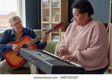 Side view portrait of Black senior woman playing piano and singing with senior man with guitar in background copy space - Powered by Shutterstock