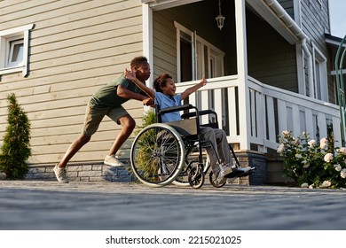 Side view portrait of black teenage boy pushing littlle brother in wheelchair while having fun together outdoors - Powered by Shutterstock