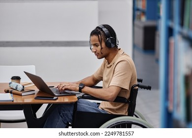 Side view portrait of black teenage boy with disability studying in college library and using laptop, copy space - Powered by Shutterstock