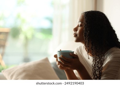 Side view portrait of a black woman at home drinking coffee and relaxing with eyes closed - Powered by Shutterstock