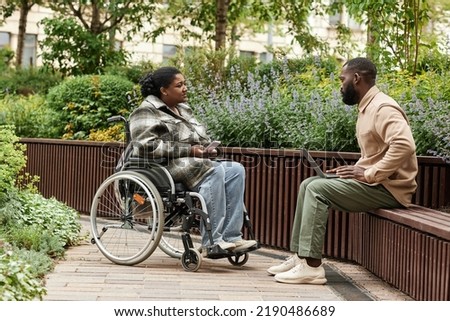 Side view portrait of black woman in wheelchair talking to friend or partner in city garden