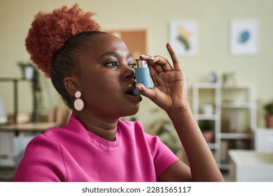 Side view portrait of black young woman using asthma inhaler at workplace in office - Powered by Shutterstock