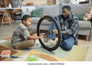 Side view portrait of Black young father and son fixing bicycle wheels together at home - Powered by Shutterstock