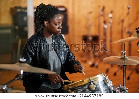 Side view portrait of black young woman playing drums in recording studio and making rock music, copy space