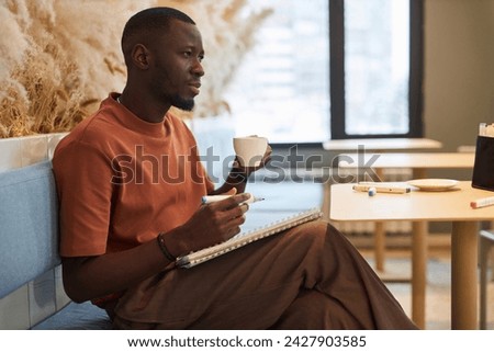 Side view portrait of Black young man as artist drawing sketches in cozy coffee shop and enjoying coffee copy space