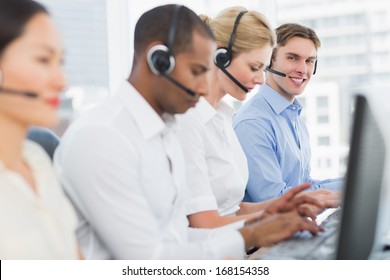 Side view portrait of business colleagues with headsets using computers at office desk