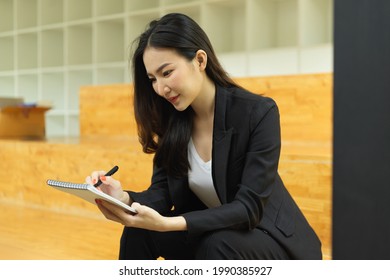 Side view portrait businesswoman in black suit writing notebook while sitting at stair case in office room