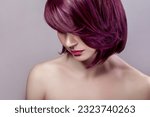 Side view portrait of calm beautiful attractive fashion model woman with short purple colored hairstyle and pink lips, looking down. Indoor studio shot isolated on gray background.