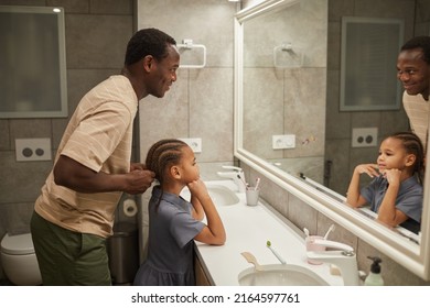 Side view portrait of caring black father braiding daughter's hair by mirror in bathroom and helping get ready in morning - Powered by Shutterstock