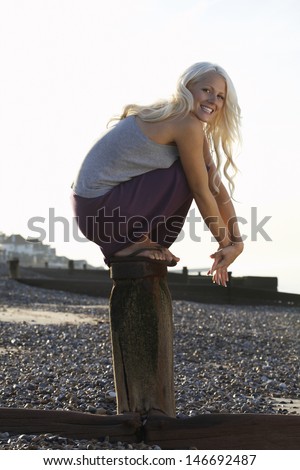 Side view portrait of cheerful young woman crouching on wooden pole at beach