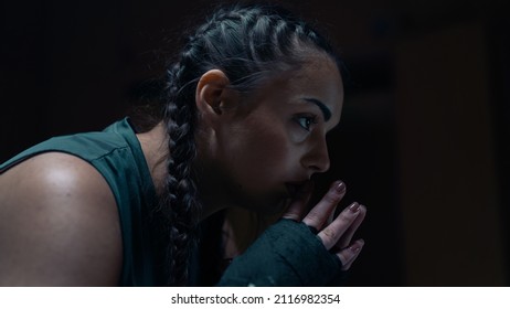 Side View Portrait Close Up Shot of an Isolated Female Kickboxer With Braids Looking Away As She Rests In Between Sparring Sessions and Kickboxing Training in an Old and Rusting Studio Gym.