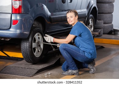 Side view portrait of confident female mechanic fixing car tire with rim wrench at garage - Powered by Shutterstock