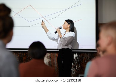 Side View Portrait Of Contemporary Businesswoman Giving Presentation Pointing At Graph Lines On Projector Screen During Lecture, Copy Space