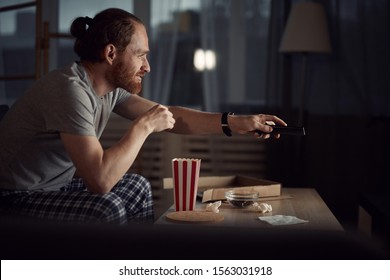 Side View Portrait Of Contemporary Man Watching TV In Dark And Eating Pop Corn While Enjoying Late Night Movies, Copy Space